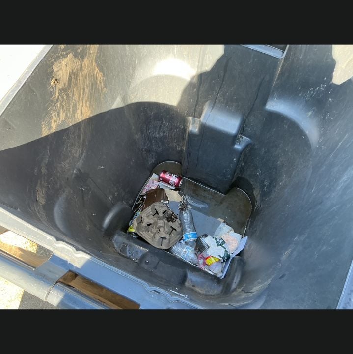 Interior of a residential trash bin before cleaning, coated in dark residue with loose trash in the base